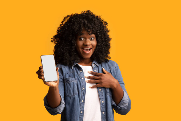 Señora negra asombrada mostrando teléfono inteligente con pantalla vacía - Foto, Imagen