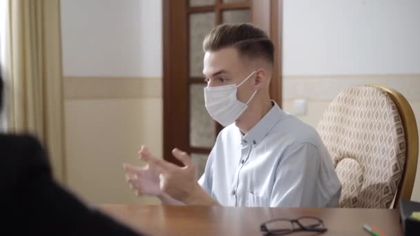 Side view portrait of stressed worried man in Covid-19 face mask gesturing and talking in psychologist office. Desperate young Caucasian guy consulting professional on coronavirus pandemic. - Séquence, vidéo