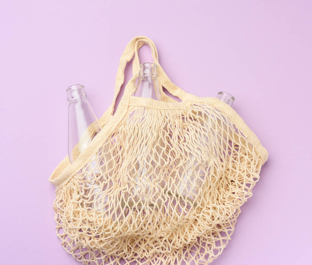 Mor arka planda boş şişeleri olan yeniden kullanılabilir tekstil alışveriş torbası, sıfır atık - Fotoğraf, Görsel
