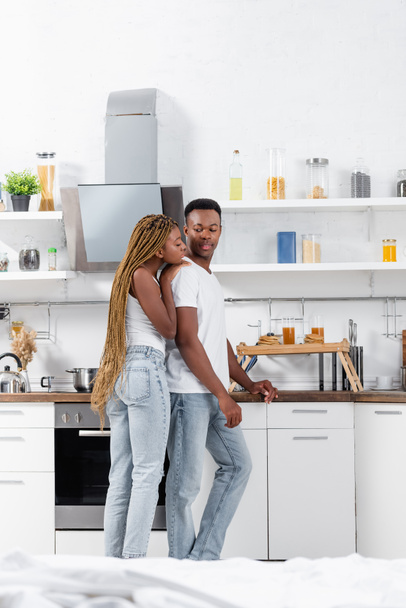 Αφροαμερικανή γυναίκα αγκαλιάζει τον φίλο της κοντά στο πρωινό στο δίσκο στην κουζίνα  - Φωτογραφία, εικόνα