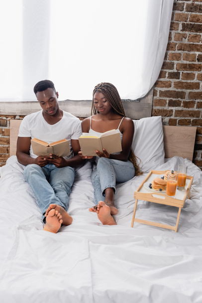 African american couple reading books near breakfast on tray on bed  - Foto, imagen