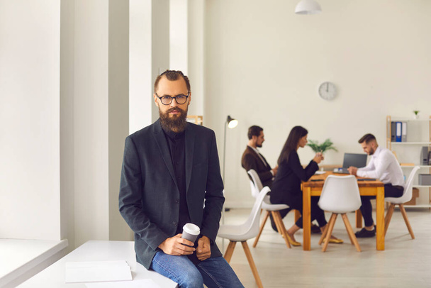 Young businessman looking at camera over colleagues sitting and working at background - Фото, зображення