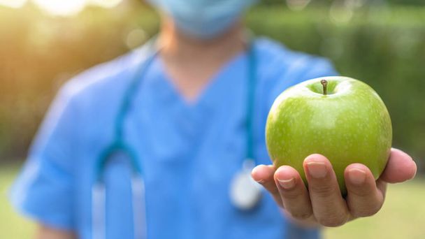 Maailman terveyspäivä, omena päivässä pitää lääkärin pois käsite terveyshyötyä syömällä runsaasti ravitsevaa puhdasta ruokaa ja terveellistä ravitsemuksellista ruokavaliota lääkäri käsittelee vihreä omena antaa potilaalle - Valokuva, kuva