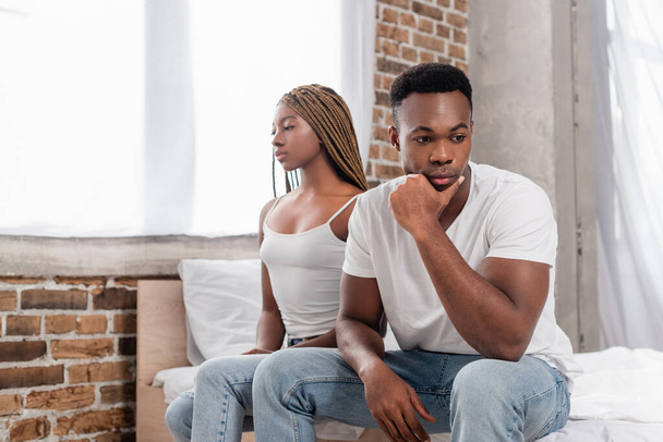 Pensive african american man sitting near girlfriend on blurred background on bed  - Fotografie, Obrázek