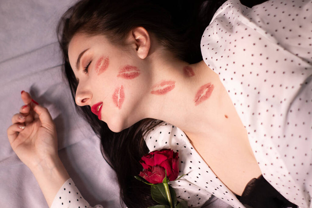 キスをしたセクシーなブルネットの女性、顔と首に口紅のマーク、赤いバラ。彼女とデートとか恋愛とか。レズビアンゲイ。ルブト。コピースペース - 写真・画像