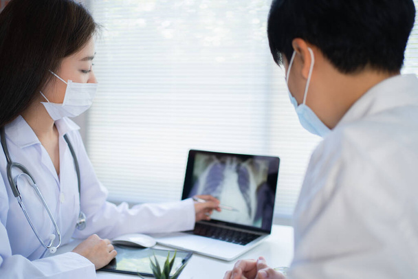 Young Asian woman doctor wearing a prophylactic mask is explaining the x-ray of the lungs in a tablet of the patient. - Photo, Image