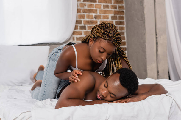 Seductive african american woman in bra touching back of shirtless man on bed  - Photo, Image