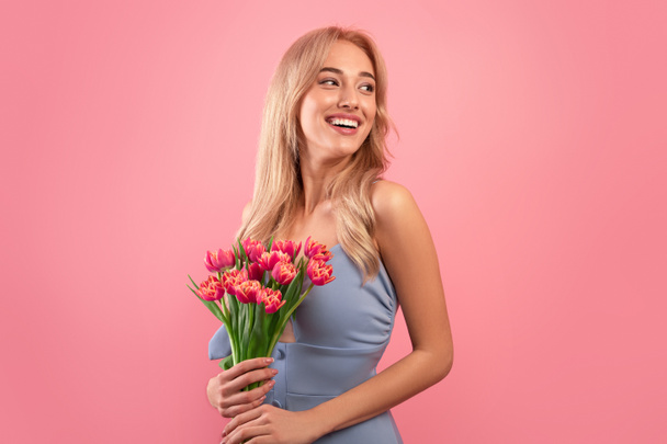 Día de la Mujer. Atractiva joven dama con un montón de tulipanes frescos celebrando las vacaciones de primavera en el fondo del estudio rosa - Foto, imagen