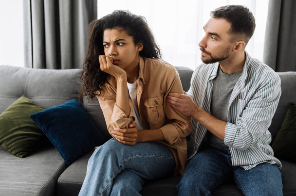 Verliebte Paare, die sich zu Hause auf der Couch über Haushalts- oder Finanzprobleme streiten. Die Frau ist von dem Mann beleidigt und ignoriert ihn. Konzept für häusliche Familienkonflikte - Foto, Bild