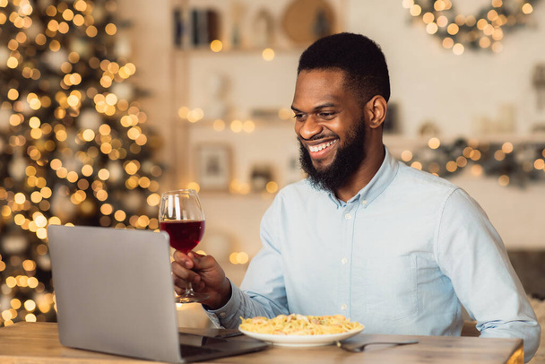 Czarny mężczyzna przy kolacji pije wino nagrywając video. - Zdjęcie, obraz