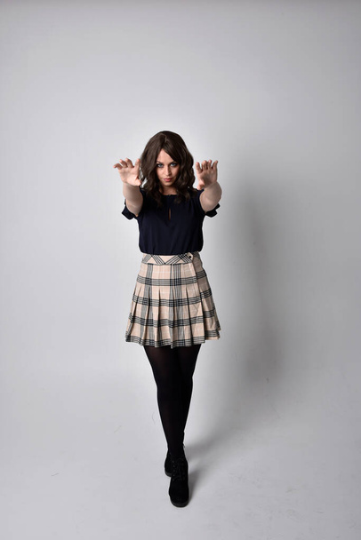 Full length portrait of pretty brunette woman wearing tartan skirt and blouse.  Standing pose on the ground,  against a  studio background. - 写真・画像