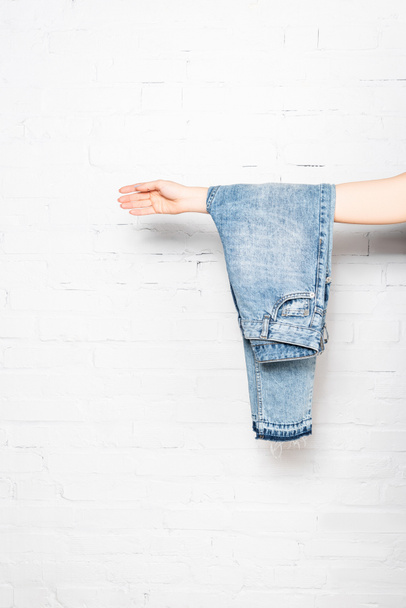 blue jeans hanging on female hand near white brick wall on background - Photo, Image
