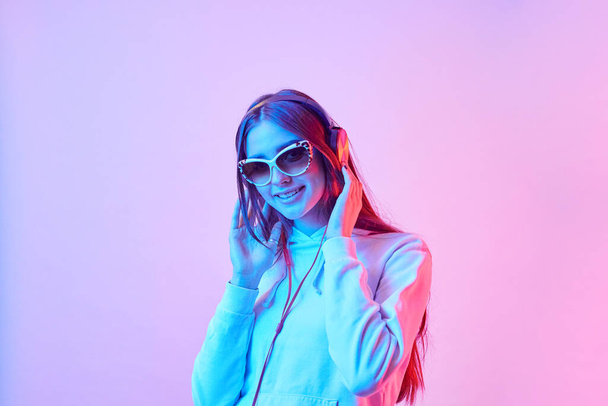 Fashion pretty girl with headphones listening to music on neon background at studio. Smiling woman. - Photo, Image