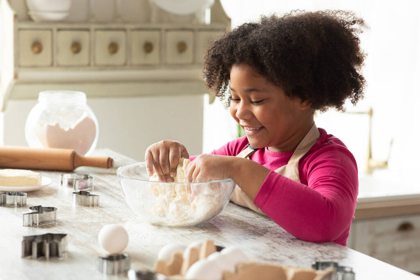 Impastatura adorabile della piccola ragazza nera per i biscotti, divertendosi in cucina - Foto, immagini