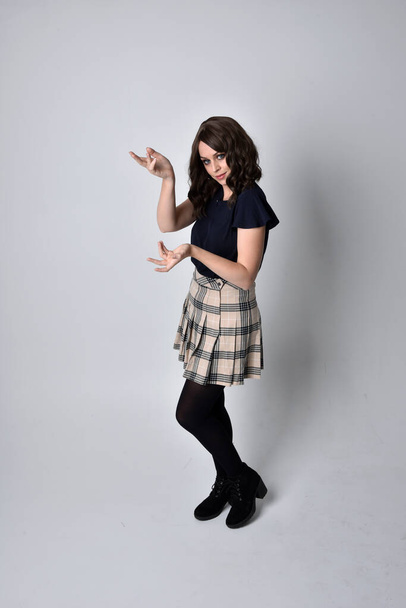Ganzes Porträt einer hübschen brünetten Frau, die Schottenrock und Bluse trägt. Standing Pose auf dem Boden, vor Studiohintergrund. - Foto, Bild