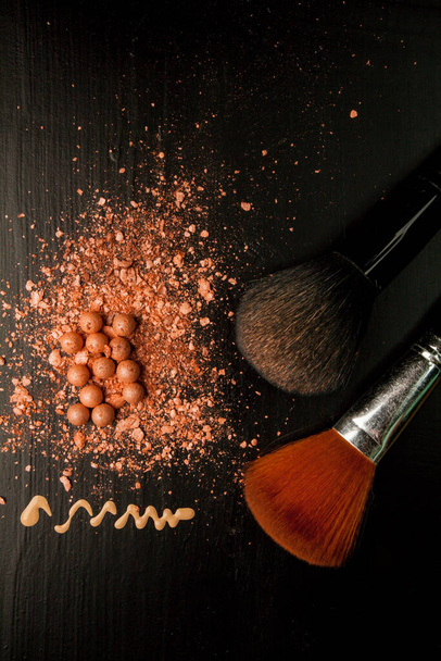Brushes for makeup on a black background with beige powder.  - Fotó, kép