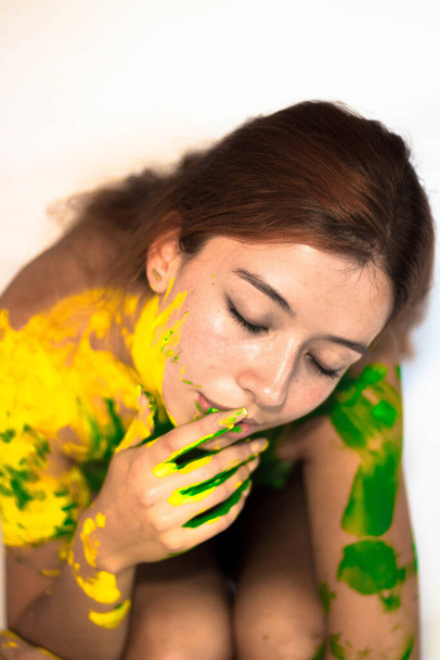 A beautiful girl with ginger hair posing while covered in yellow and green paint - Fotografie, Obrázek