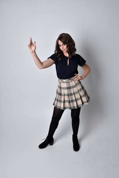 Ganzes Porträt einer hübschen brünetten Frau, die Schottenrock und Bluse trägt. Standing Pose auf dem Boden, vor Studiohintergrund. - Foto, Bild
