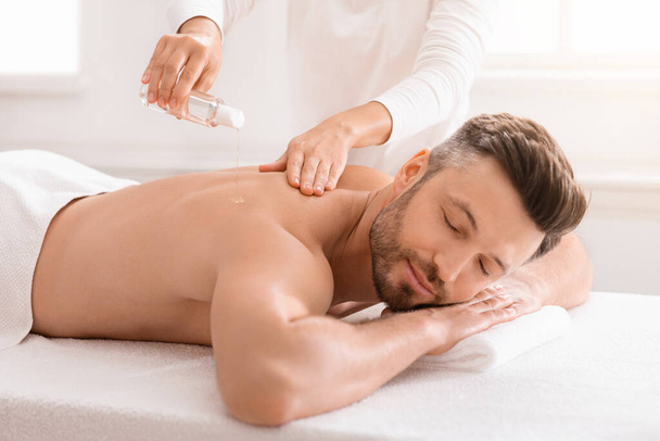 Irriconoscibile massaggiatrice versando olio sull'uomo indietro - Foto, immagini