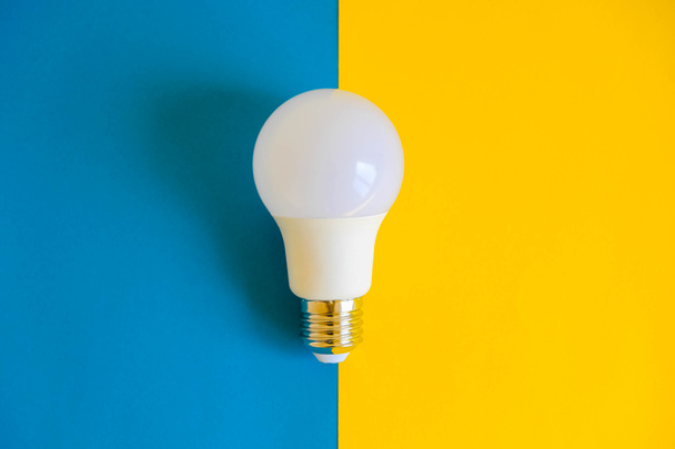LED light bulb on blue and yellow background. Top view. Copy, empty space for text. - Photo, Image