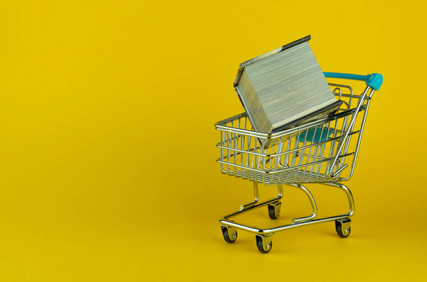 A little metallic cart and a tiny book on a yellow surface and background - copy space - Foto, afbeelding
