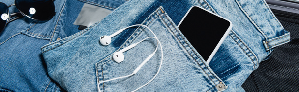 крупный план мобильного телефона в кармане джинсов возле наушников и солнцезащитных очков, баннер - Фото, изображение