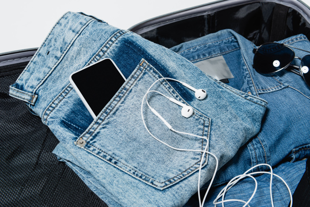 top view okostelefon zsebében farmer közelében fülhallgató, farmer ing és napszemüveg csomagolt utazási táska - Fotó, kép