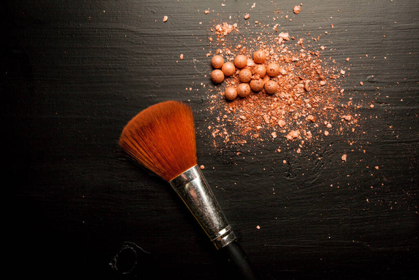 Brushes for makeup on a black background with beige powder.  - Fotó, kép