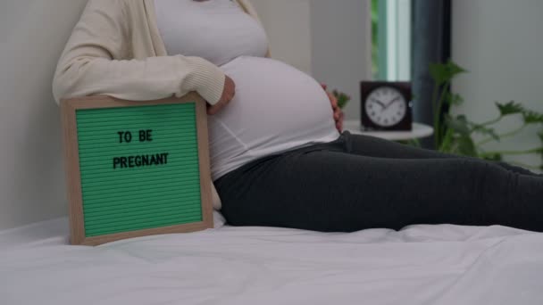 Šťastná matka a připravit těhotnou koncepci.Těhotné ženy vidět "být těhotná" Na zelené desce. žena se připravuje deska pro focení a příspěvek na sociálních sítích ukazující její těhotenství.  - Záběry, video