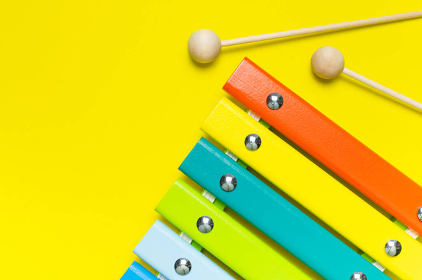 多色の木製の木琴と衝撃は、明るい黄色の背景フラットレイアウト上のビューのコピースペースに固執します。木製の子供の音楽おもちゃ赤ちゃん楽器虹の色。子供の自然エコおもちゃ. - 写真・画像