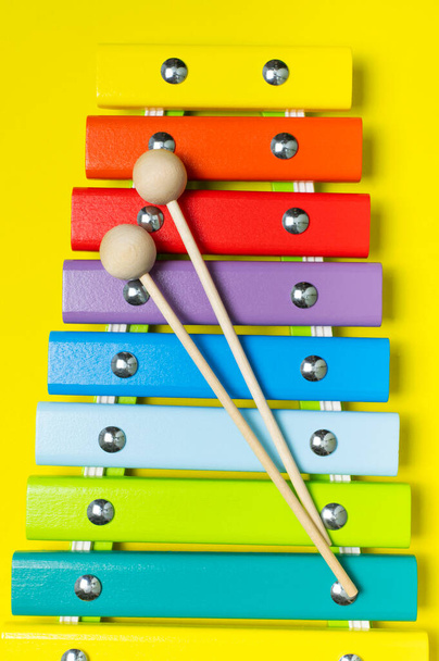 Multicolored wooden xylophone and shock sticks on bright yellow background flat lay top view copy space. Wooden children's musical toy Baby musical instrument Colors of rainbow. Kids natural eco toys. - Fotó, kép
