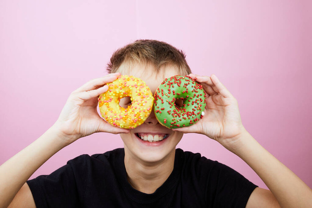 Happy boy is having fun played with donuts on pink background. Child holds doughnut glasses. Close up. - Foto, Imagen