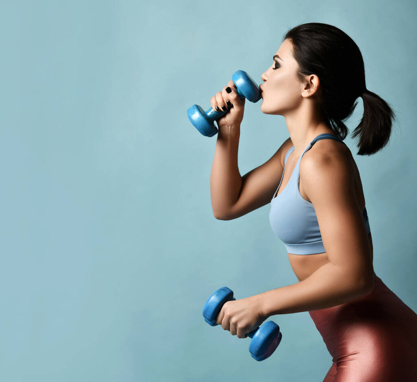 Young beautiful fitness brunette woman in sportswear kissing dumbbell during sports training - Photo, image