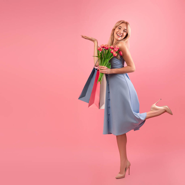Blond dametje met tulpen en boodschappentassen met iets op roze achtergrond, model voor uw productontwerp - Foto, afbeelding