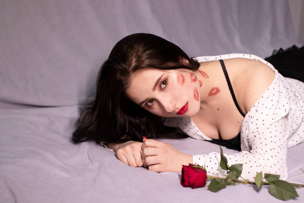 Seksowna brunetka z pocałunkami, ślady szminki na twarzy i szyi, z czerwoną różą. Dziewczyna, randka, relashionship. przestrzeń kopiowania - Zdjęcie, obraz