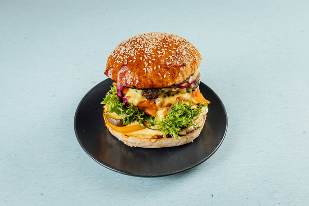 A closeup of a delicious burger with pickles and melted cheese on a plate - 写真・画像