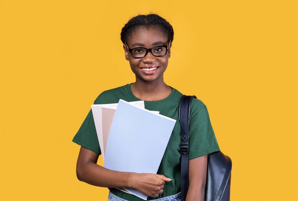 Feliz estudiante negra posando con libros sobre fondo amarillo - Foto, imagen