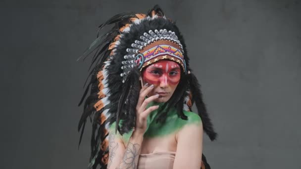 Modelo femenino tatuado posa con tocado indio en fondo oscuro - Imágenes, Vídeo