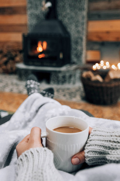 A shallow focus shot of hands holding a mug of coffee on fireplace backgrou - Foto, immagini