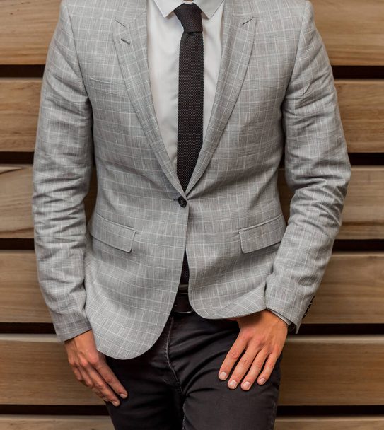 A male in an elegant elegant classic gray suit leaning on a wooden wall - Φωτογραφία, εικόνα