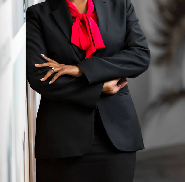 A selective focus of a businesswoman in a classic black suit and red shirt with her arms crossed - Foto, Bild