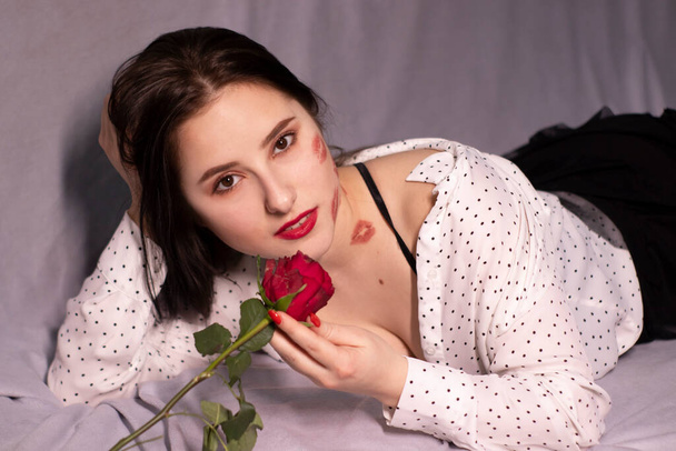 sexy brunette woman with kisses, lipstick marks on her face and neck, with red rose. girlfriend, date, relashionship. copy space - Photo, Image