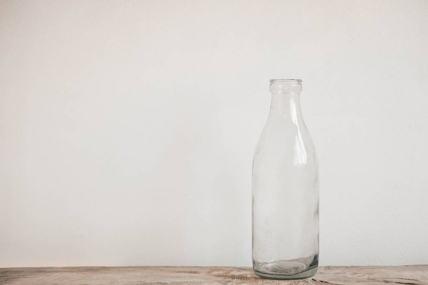Стеклянная прозрачная бутылка на деревянном столе на белом фоне стены. Копирование, пустое место для текста. - Фото, изображение