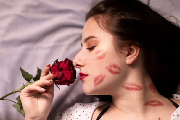 sexy brunette woman with kisses, lipstick marks on her face and neck, with red rose. girlfriend, date, relashionship. copy space - Photo, image