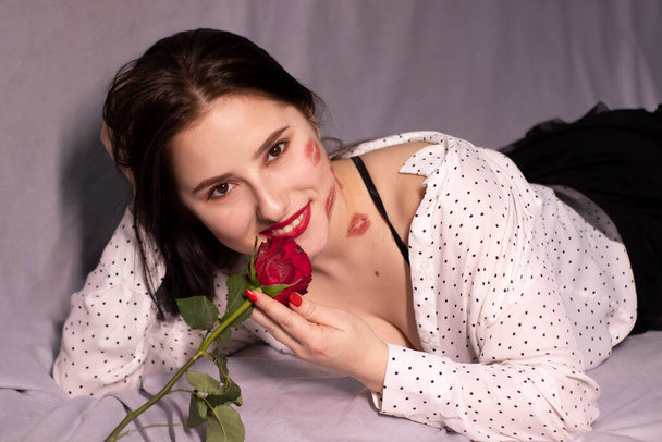 sexy brunette woman with kisses, lipstick marks on her face and neck, with red rose. girlfriend, date, relashionship. copy space - 写真・画像