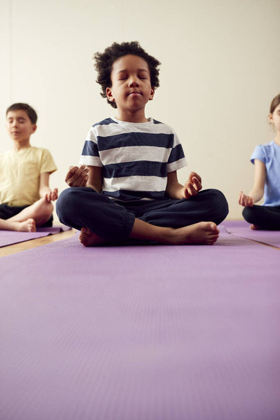 Group Of Children Sitting On Exercise Mats And Meditating In Yoga Studio - Foto, afbeelding