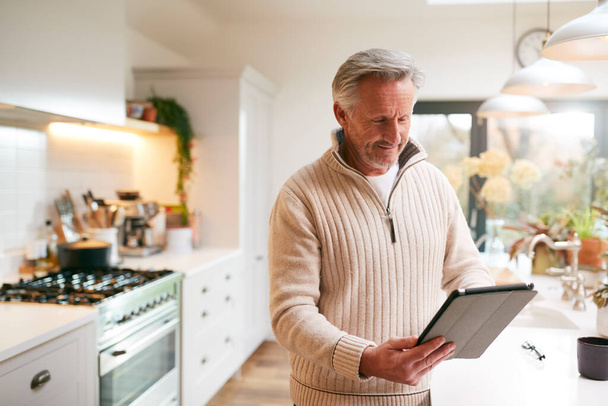 Mature Man In Kitchen Working From Home Using Digital Tablet - Photo, Image
