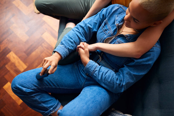 Loving Same Sex Female Couple Holding Hands Lying On Sofa At Home Watching TV And Relaxing Together - 写真・画像