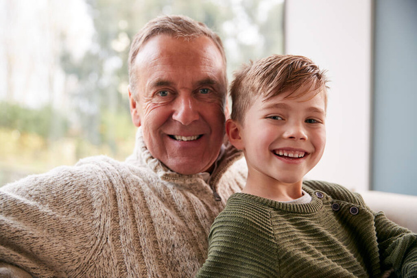 Portrait Of Grandson Sitting On Sofa At Home With Grandfather - Photo, image