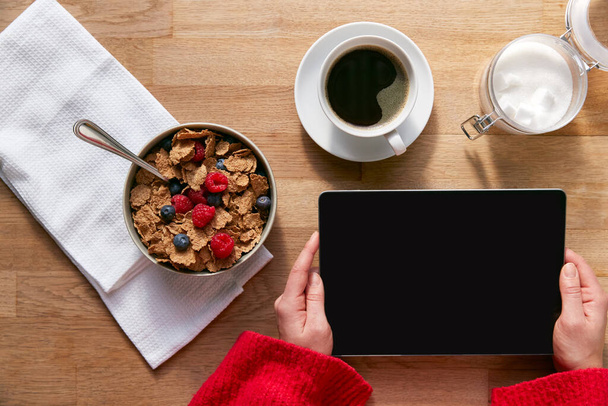 Overhead Flat Lay Of Woman Using Digital Tablet On Table Laid For Breakfast With Cereal And Coffee - Fotoğraf, Görsel